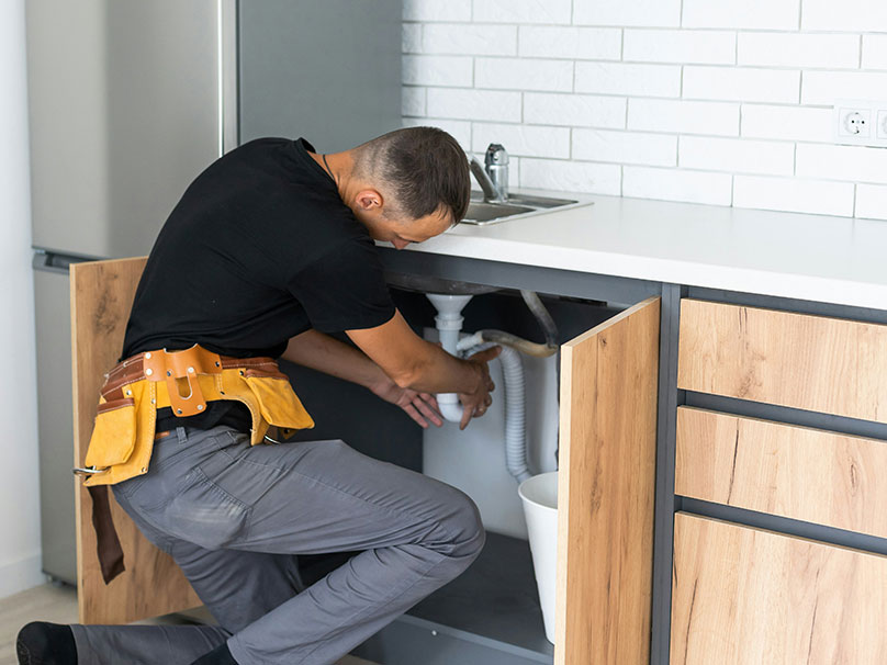 Man working under a sink to repair a drain