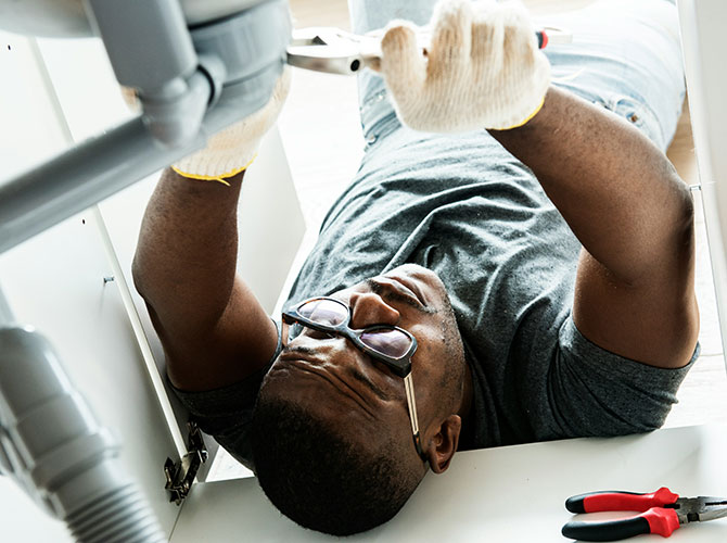 Man laying under a sink working on a drain above him